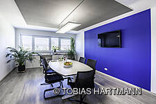 Besprechungsraum mit blauer Wand, ovalem Tisch und Bildschirm